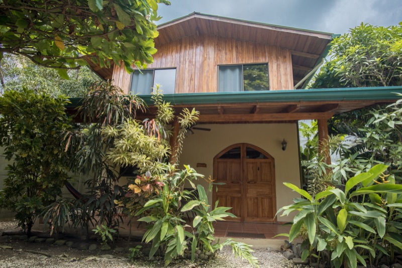 2-story wooden villa with a green roof and arched front doors behind tropical plants at Villas Solar