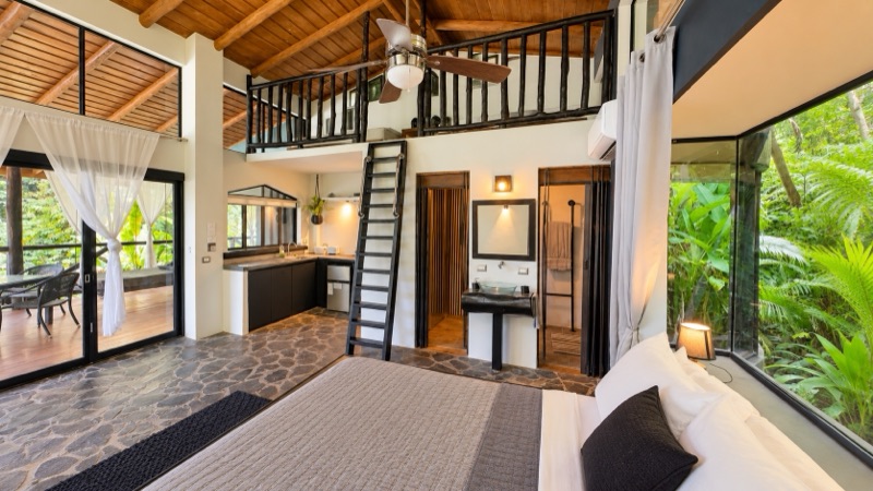 Open-plan room with stone floor, loft ladder and jungle-view windows at Canaima Chill House