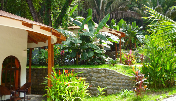 White rounded bungalows with wooden porches among banana plants and flowering gardens at Hotel Manalá