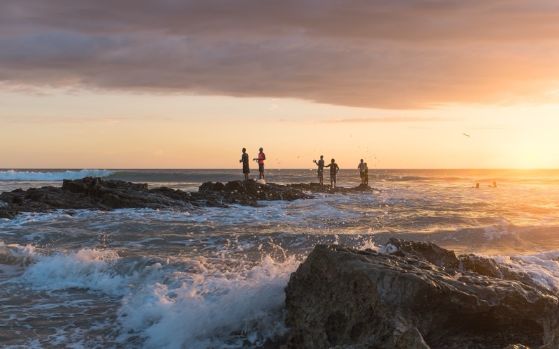 Fishermen standing on rocks at sunset as waves break on Playa Santa Teresa
