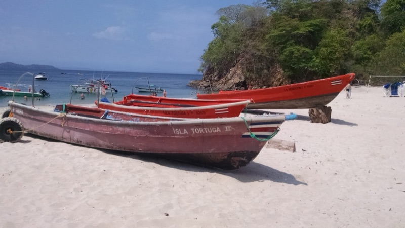 Red wooden boats pulled up on the white sand at Isla Tortuga